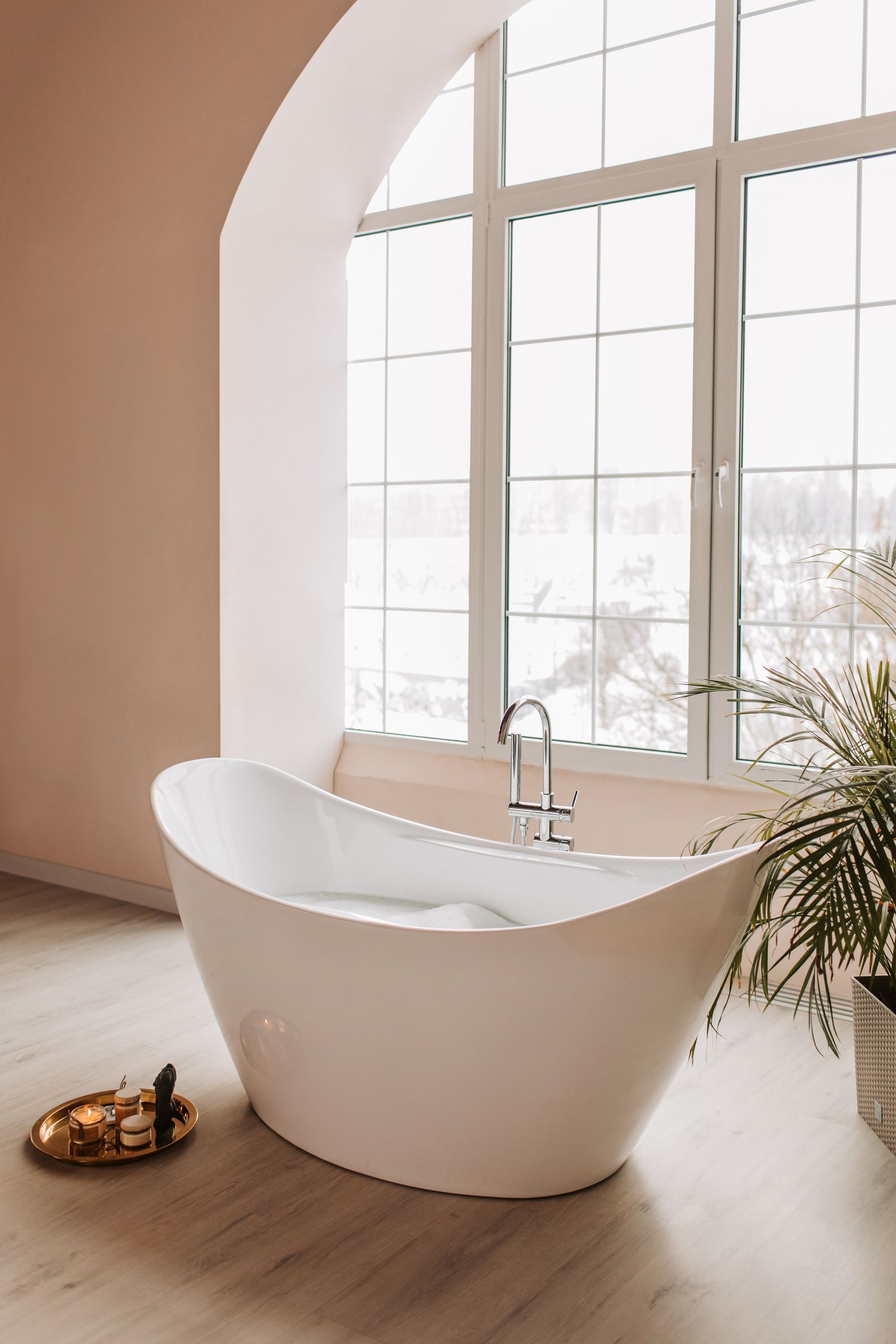 A calm, naturally lit bathroom with a freestanding tub beside a tall window